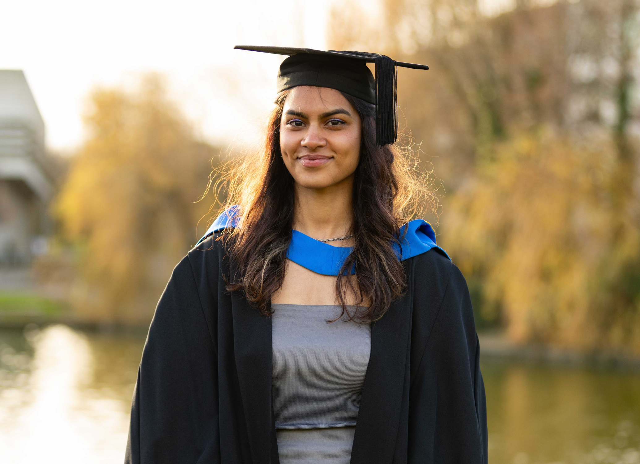 UCD alumna Jessica Ann George wearing graduation cap and gown, posing for a photo by the main UCD lake.
